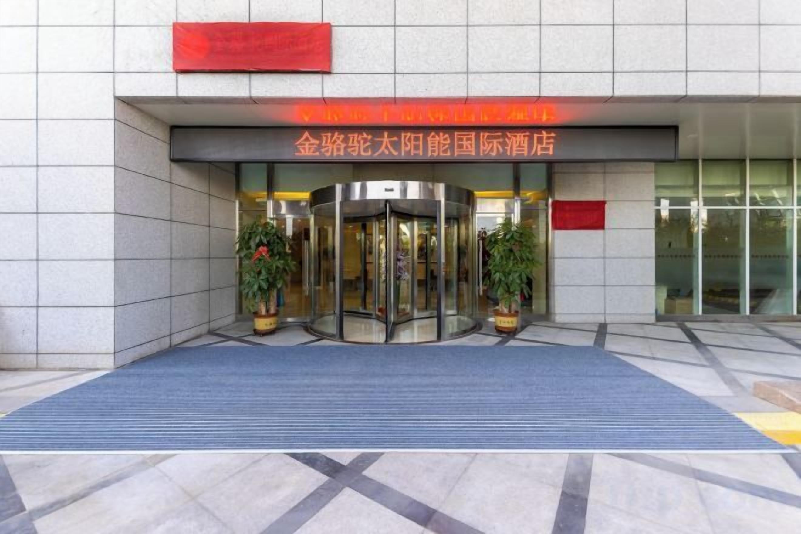 A hotel entrance with a revolving door, potted plants, and a red sign above.