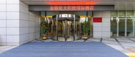 A hotel entrance with a revolving door, potted plants, and a red sign above.