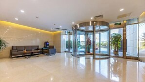 Eine moderne Lobby mit einer Glastür, die sich drehen kann, einem Sofa, einem kleinen Tisch und einer Topfpflanze.