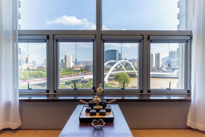 Ein Zimmer mit großem Fenster und Blick auf eine Stadtlandschaft, einschließlich einer Brücke und Gebäuden.