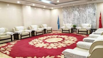 Un salón de conferencias con alfombra roja, filas de sillas blancas y banderas.