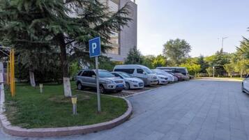 A parking area with a blue parking sign, lined with parked cars, and a building with a modern design in the background.