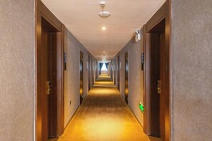Een hotelgang met deuren aan weerszijden, een vloerbedekking en een plafondlamp.