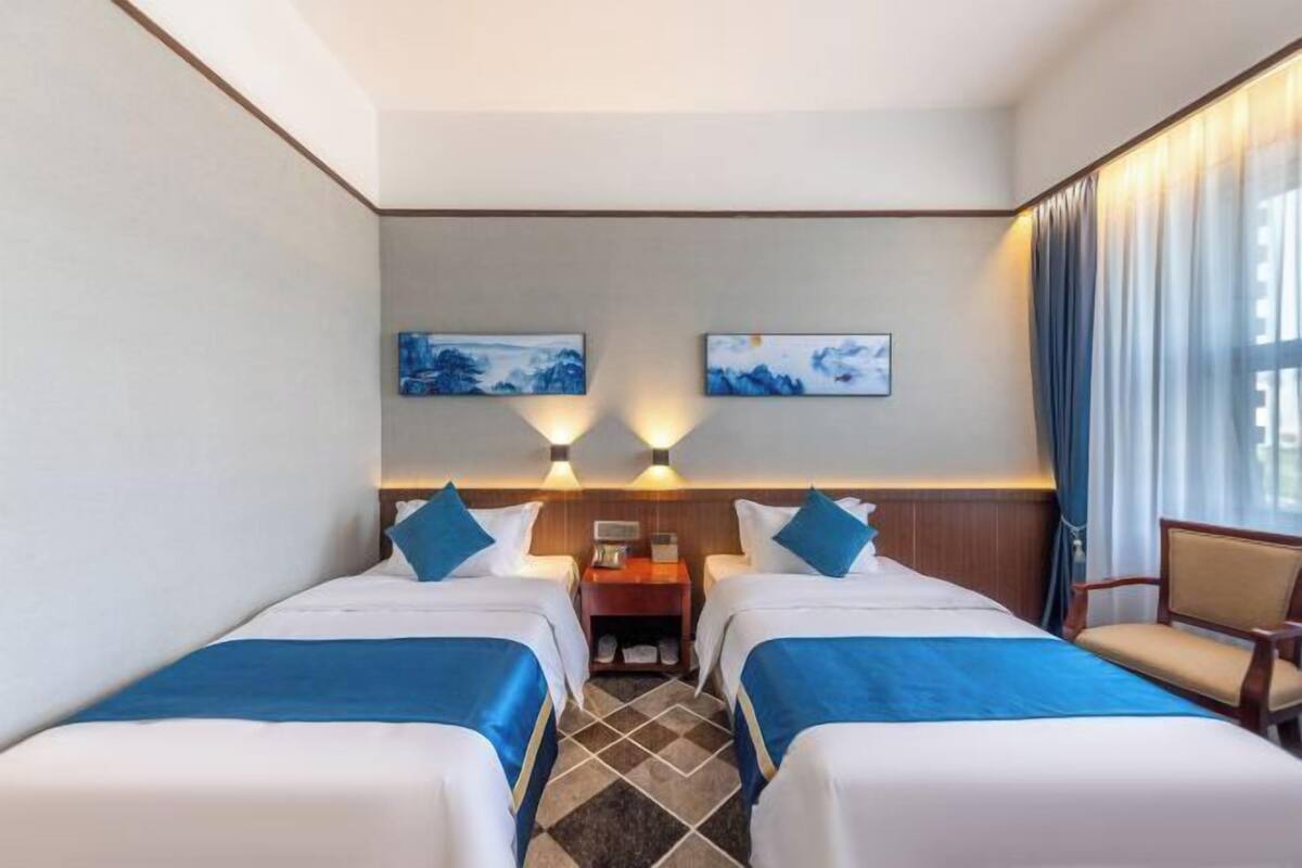 A hotel room with two beds, a nightstand, a chair, and artwork on the wall.