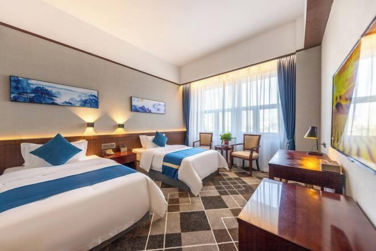 A hotel room with two beds, a desk, a chair, and a small table.