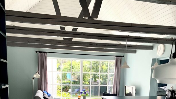 A spacious kitchen with a large window, a dining area with a sofa, and a white table.