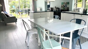 A modern kitchen with white cabinetry, a dining table, and chairs. There is a window providing natural light and a view of the outdoors.