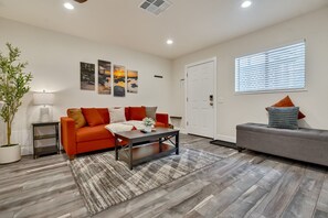A modern living room with a sofa, a coffee table, and a grey couch. There is a door and a window with blinds.