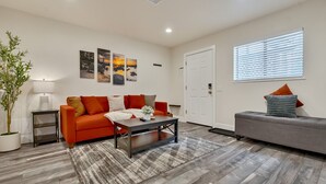 A modern living room with a sofa, a coffee table, and a grey couch. There is a door and a window with blinds. - Walk to Kings Beach | Summer Cabin Retreat! (Kings Beach)