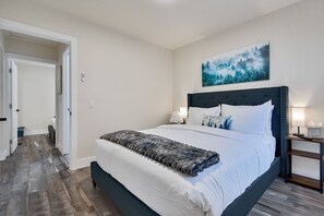A bedroom with a large bed, a dark headboard, a painting of a forest, and a wooden floor. - Kings Beach Cabin | 5-Min Walk to Sand & Shops (Kings Beach)