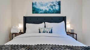 A neatly made bed with white linens, a dark headboard, and a forest-themed pillow. There are two bedside lamps on either side of the bed. - Walk to Kings Beach | Summer Cabin Retreat! (Kings Beach)