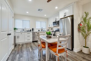 A modern kitchen with white cabinetry, stainless steel appliances, and a dining area with a wooden table and chairs. - Kings Beach Cabin | 5-Min Walk to Sand & Shops (Kings Beach)