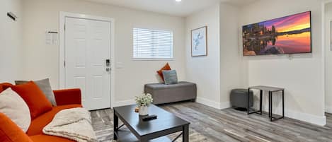 A modern living room with a sofa, ottoman, coffee table, and a painting on the wall.
