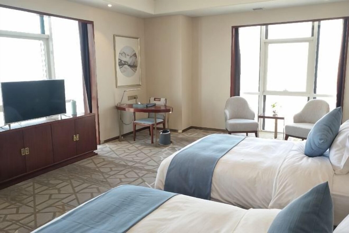 Una habitación de hotel con dos camas, un escritorio, un televisor y una ventana.