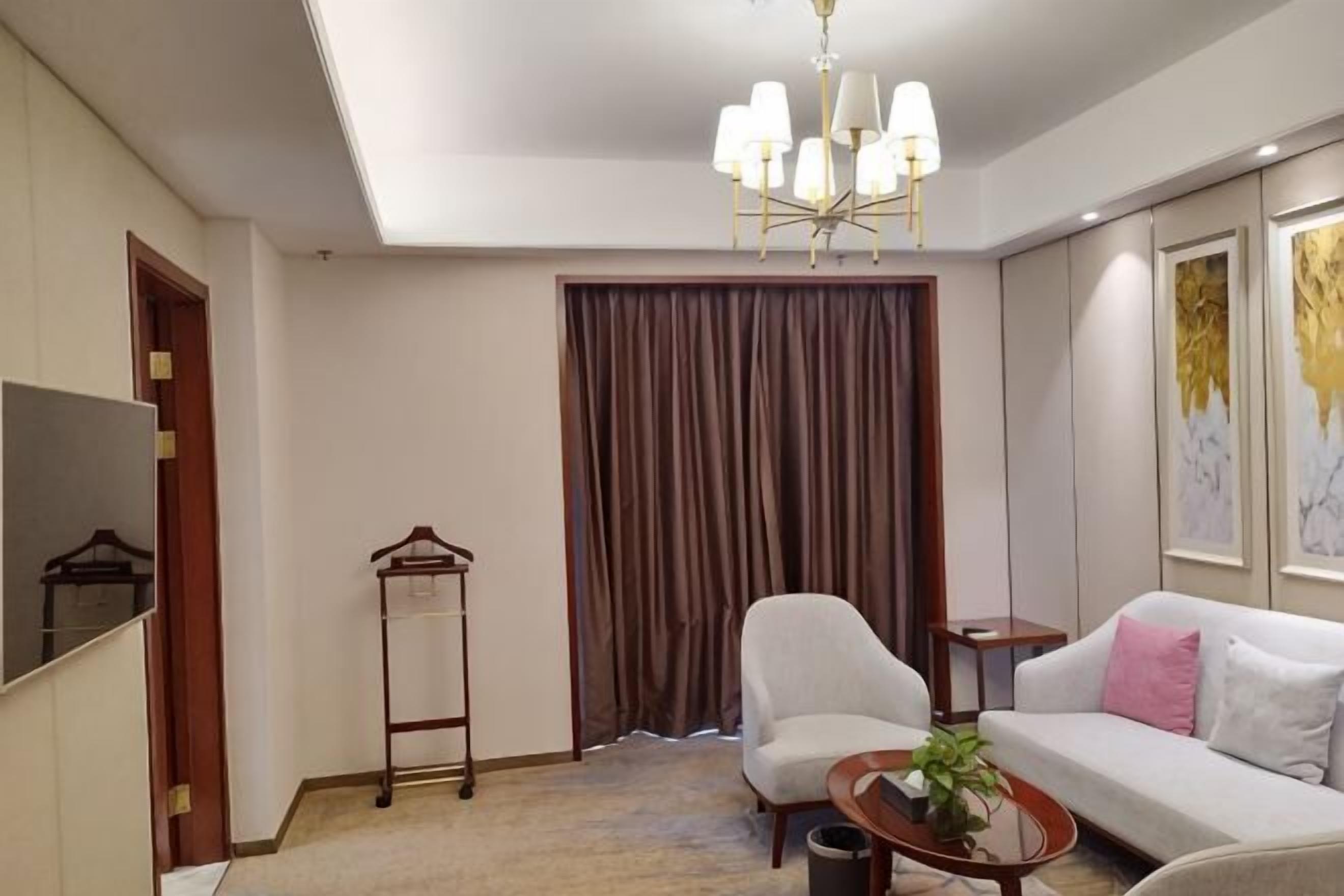Una habitación de hotel con sofá, sillón, lámpara colgante y perchero.