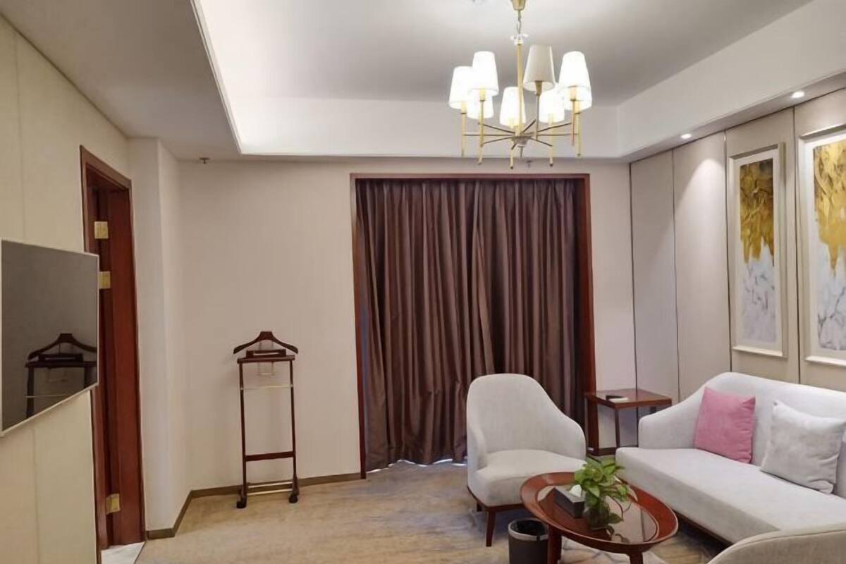 Une chambre d’hôtel équipée d’un canapé, d’un fauteuil, d’un luminaire suspendu et d’un porte-manteau.