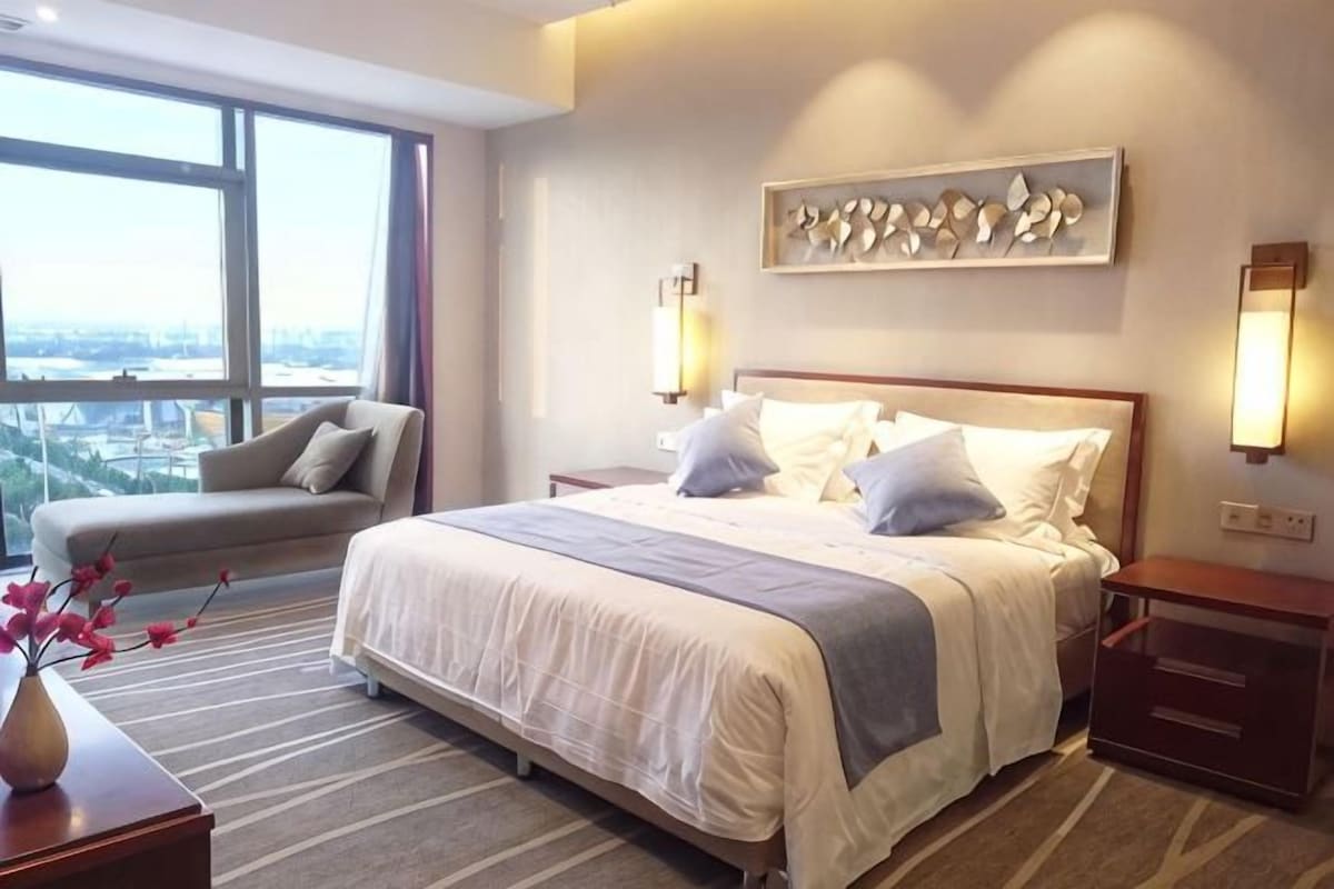 Habitación de hotel con una cama grande, un sofá, vistas de la ciudad y un cuadro en la pared.