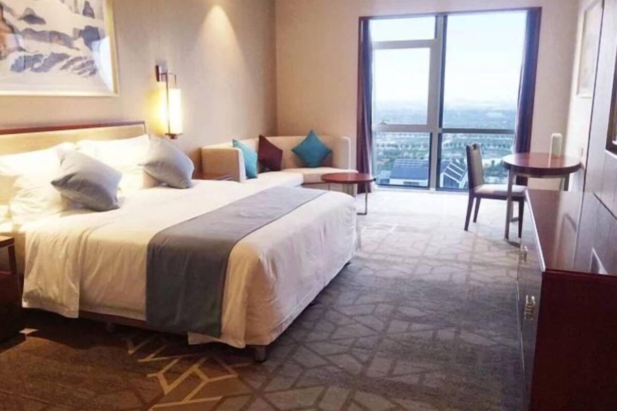 Une chambre d’hôtel avec un grand lit, un bureau, une chaise et une vue sur la ville grâce à une grande fenêtre.
