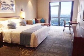 Hotelkamer met een groot bed, een bureau, een stoel en uitzicht op de stad door een groot raam.