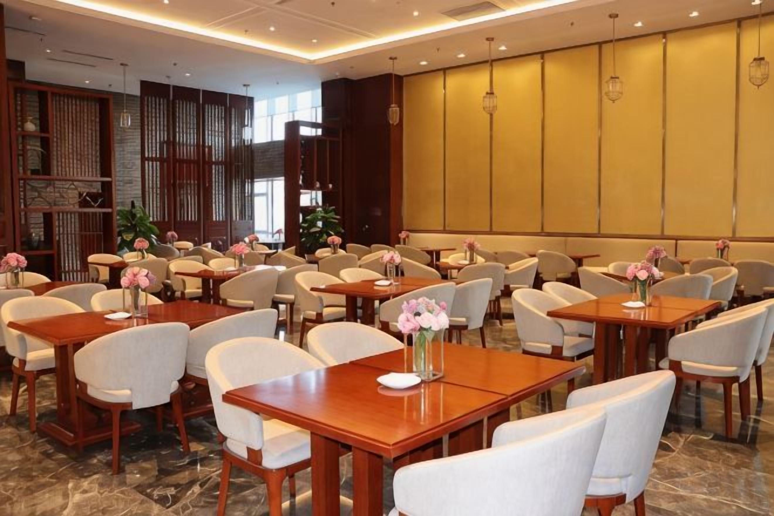 A hotel dining area with multiple tables and chairs, some with floral centerpieces.