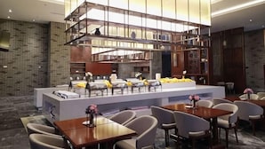 A modern restaurant with a central island, seating around it, and a unique hanging light fixture. - Feng Du Hotel (Dezhou)