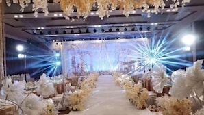 A venue with a central aisle flanked by tables, overhead floral decorations, and a stage with bright lights. - Feng Du Hotel (Dezhou)