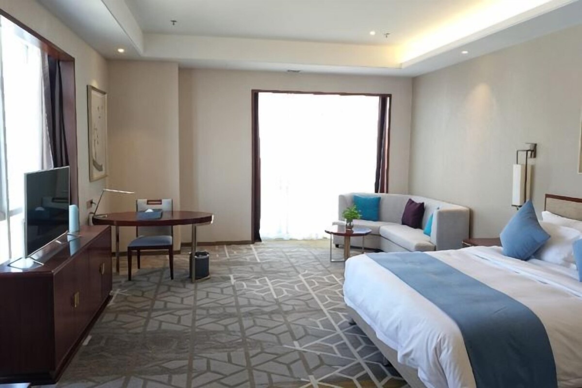 Una habitación de hotel con cama, escritorio, silla, sofá y televisor.