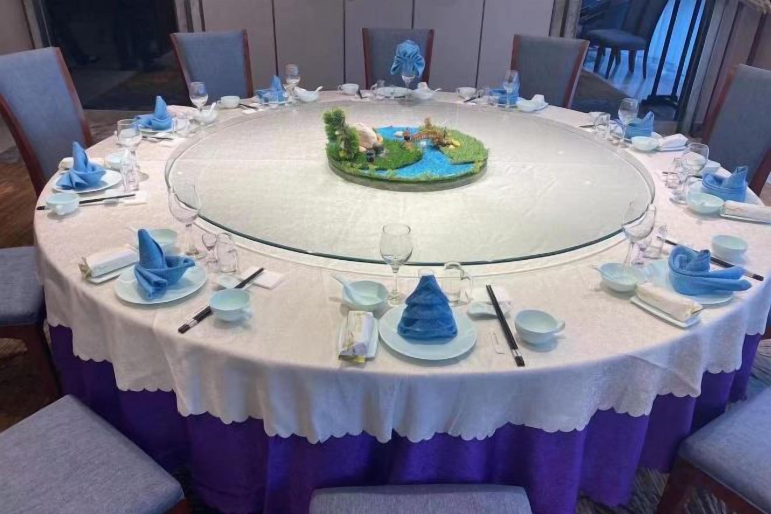 Une table ronde avec un îlot central, entourée de chaises et dressée avec des serviettes, des assiettes et des verres bleus.