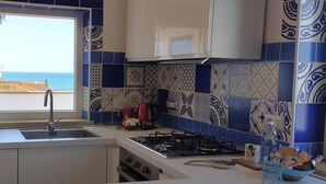 A kitchen with a view of the sea, a microwave, a sink, and a gas stove. - Sea view penthouse for 2-4 people, large equipped terrace (anzio)
