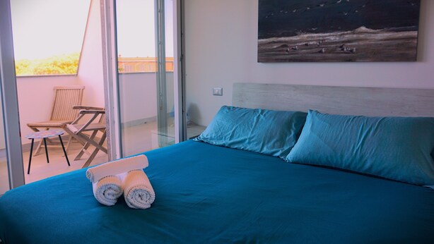 A bedroom with a bed, a painting, and a view of the outside. - Apartment for family with children, 200 mt from the sea (anzio)