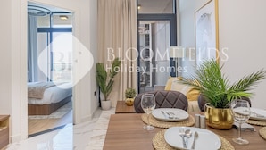 Ein modernes Hotelzimmer mit einem Bett, einem Essbereich mit Tisch für zwei Personen und einem großen Fenster mit Vorhängen.