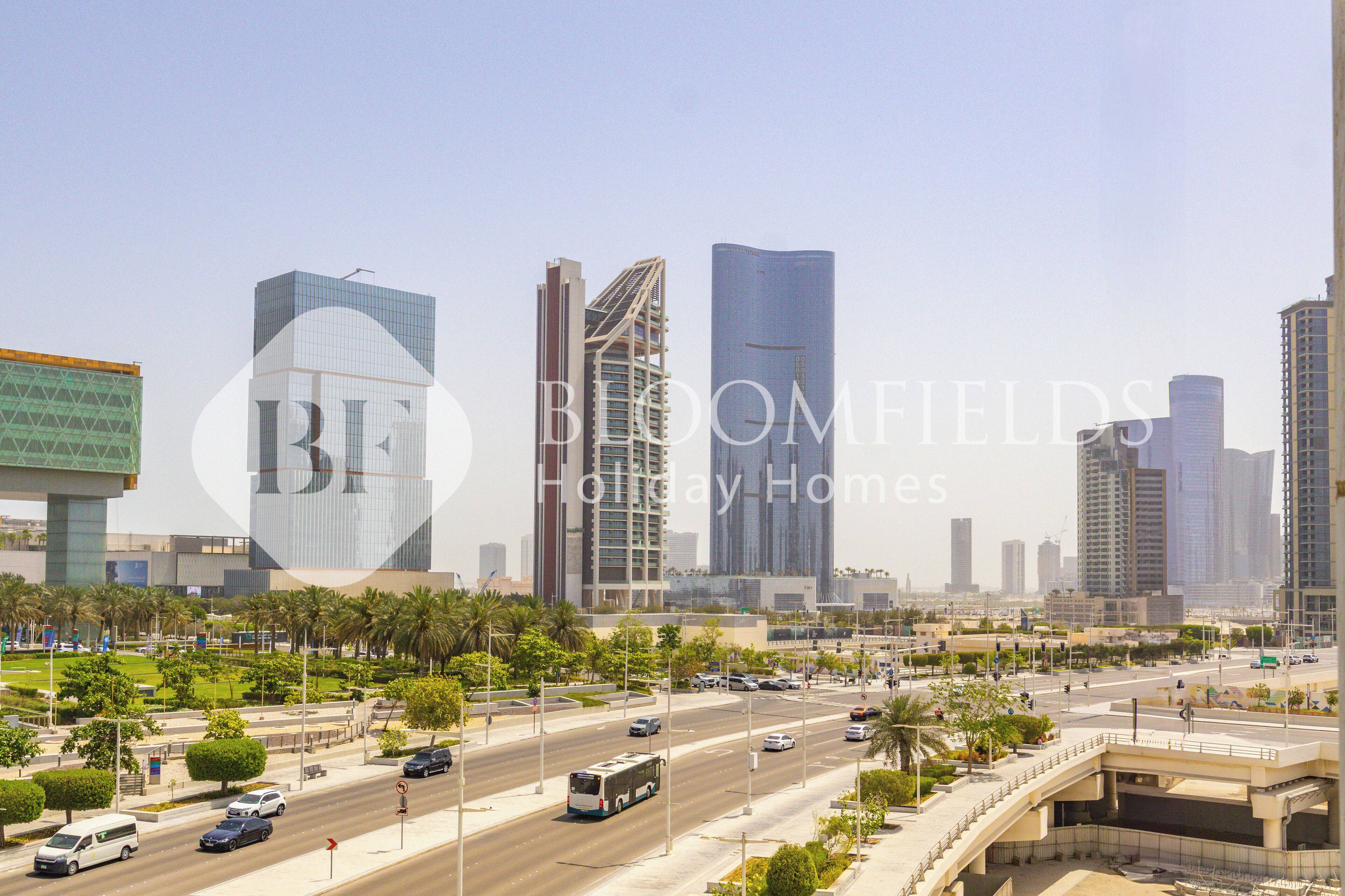 A cityscape with modern high-rise buildings, a busy road, and palm trees.