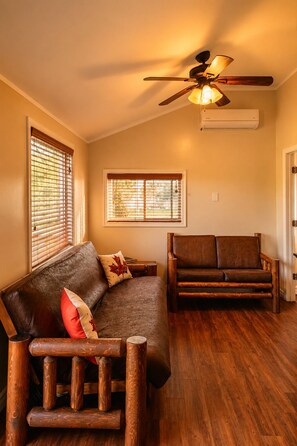Quarto com piso de madeira, ventilador de teto e dois sofás de madeira.