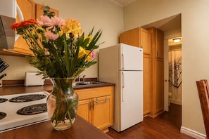 Eine Küche mit Holzschränken, einem weißen Kühlschrank, einem Herd und einer Vase mit Blumen auf der Arbeitsplatte.