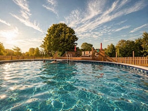Une piscine à l’eau claire, entourée d’une terrasse en bois, d’un grand arbre et d’une clôture en bois.