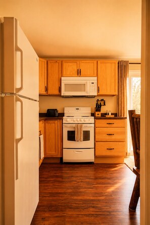 A compact kitchen with wooden cabinets, a microwave, an oven, and a refrigerator.
