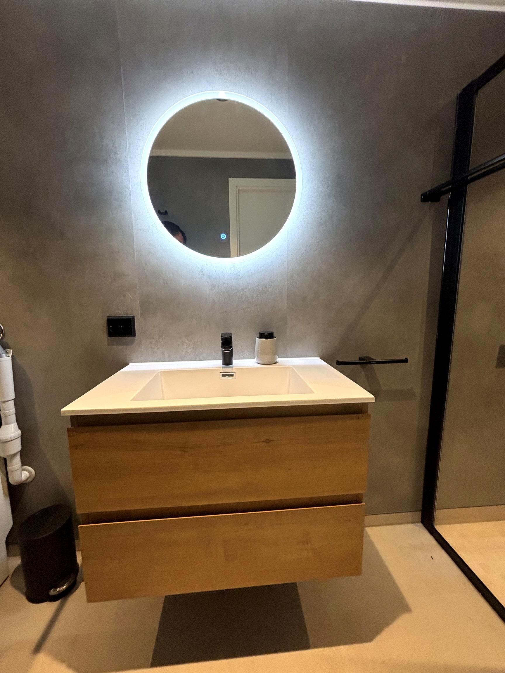 Une salle de bain moderne avec un miroir rond, un meuble-lavabo en bois et une porte de douche noire.