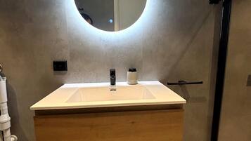 Une salle de bain moderne avec un miroir rond, un meuble-lavabo en bois et une porte de douche noire.