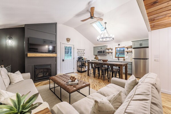 Una sala de estar moderna con chimenea, un comedor y una cocina con refrigerador de acero inoxidable.