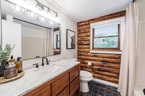 Un baño con pared de madera, un espejo grande y una ventana con vistas a árboles.