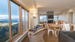 Amplia sala de estar con un gran ventanal que ofrece vistas del paisaje, una chimenea y un comedor con muebles de mimbre.