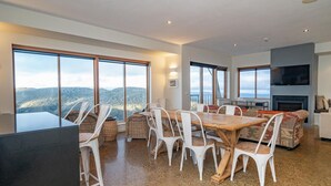 Un espacio habitable amplio con una gran mesa de madera y sillas blancas, una chimenea y un televisor montado en la pared.