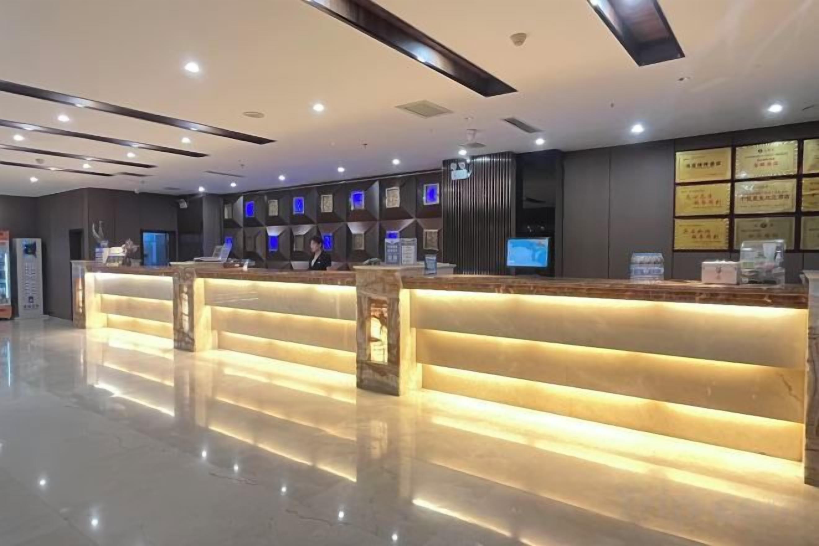 A hotel reception area with a modern design, featuring a long reception desk with integrated lighting, multiple monitors, and a clean, polished floor.