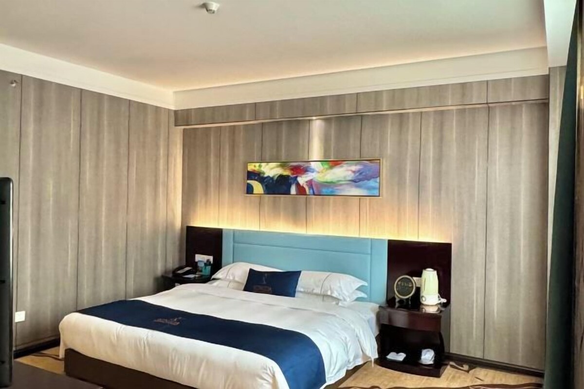 Ein Hotelzimmer mit einem großen Bett, einem Nachttisch mit Lampe und einem Gemälde an der Wand.