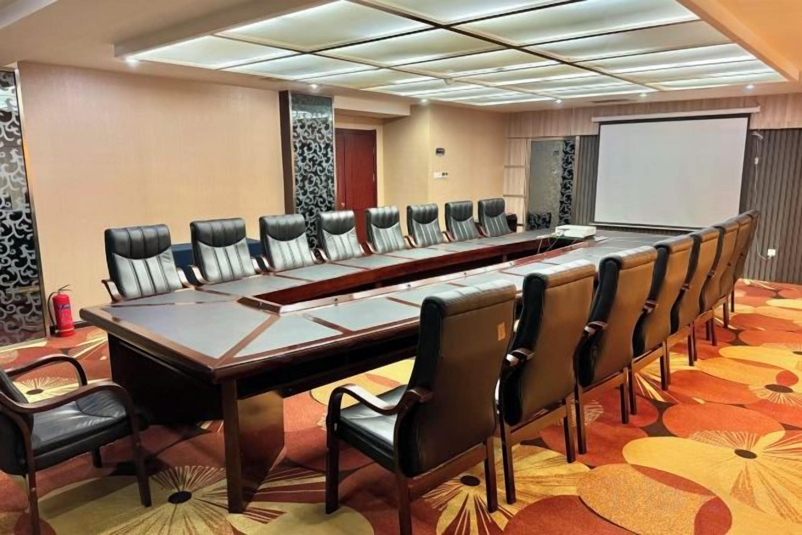 A conference room with a long table and chairs, a projector screen, and a carpeted floor.