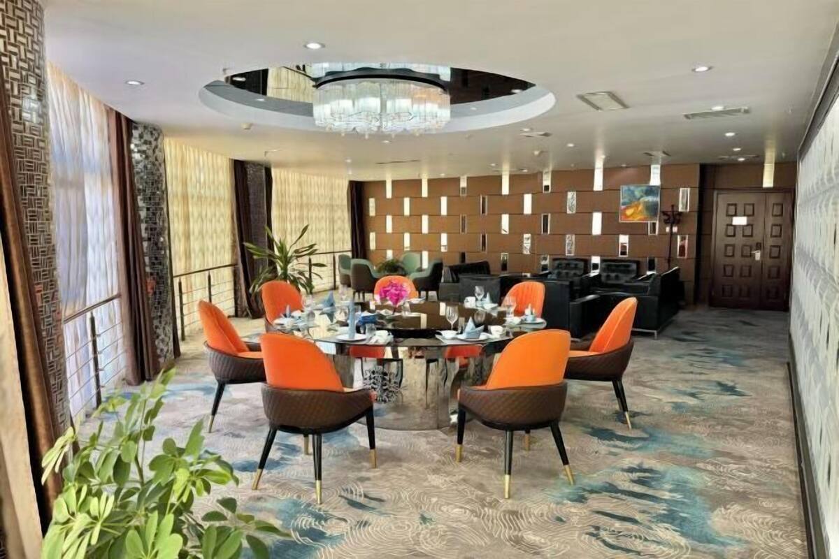 Un coin repas avec une table ronde, des chaises orange et un lustre.
