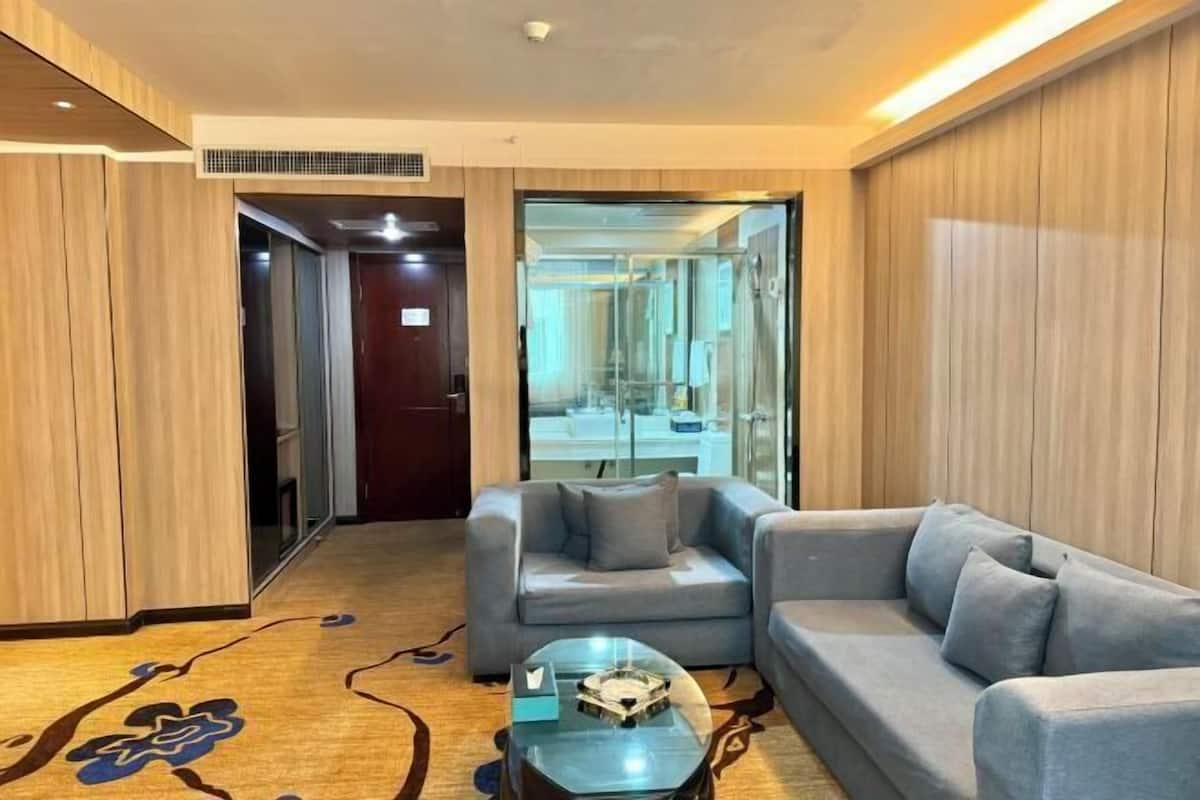 Une chambre d’hôtel moderne avec un canapé gris, une table basse en verre et un plancher en bois orné d’un motif floral.