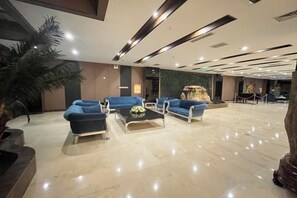 Um hall amplo com área de estar, sofás e uma mesa de centro, uma planta grande e um balcão de recepção.