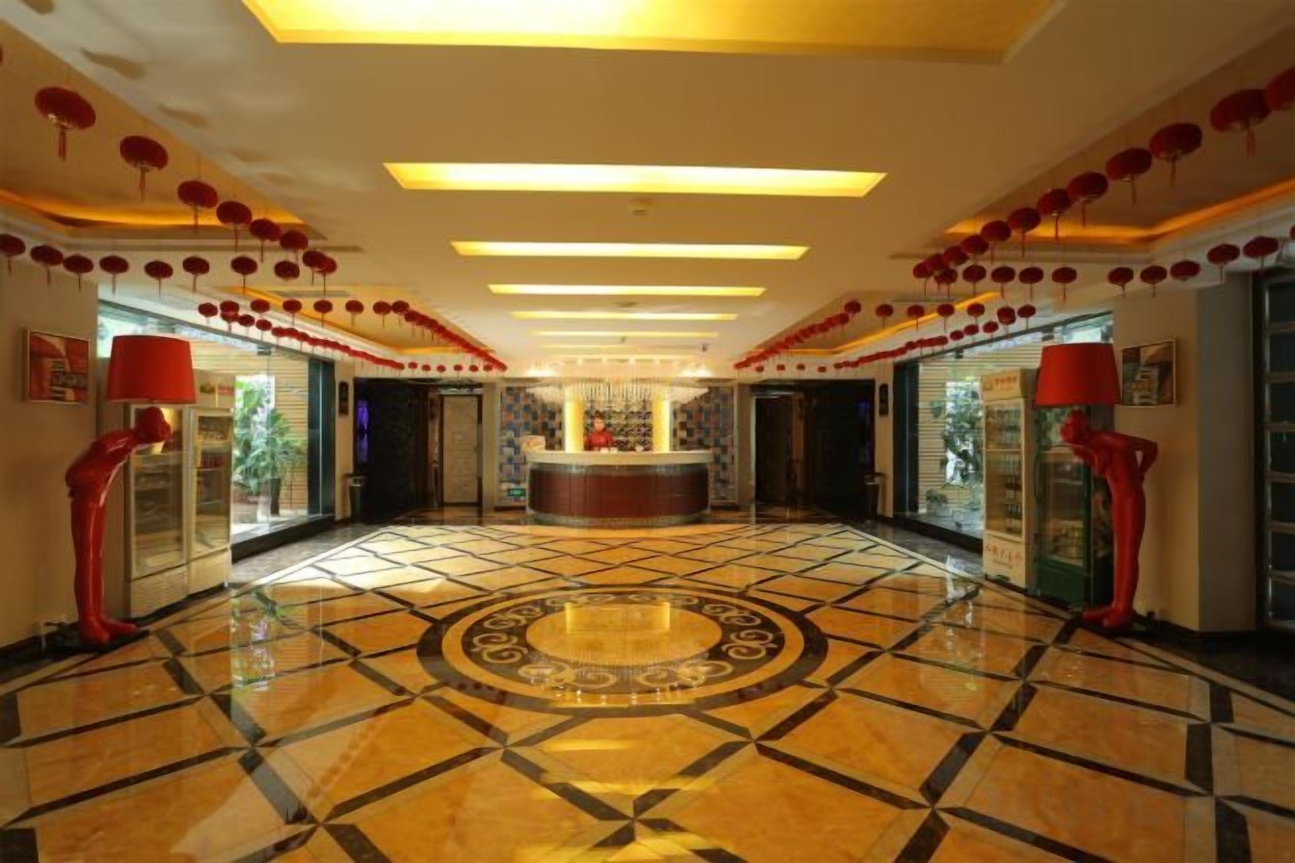 A hotel lobby with a central reception desk, patterned floor, and red decorative elements.