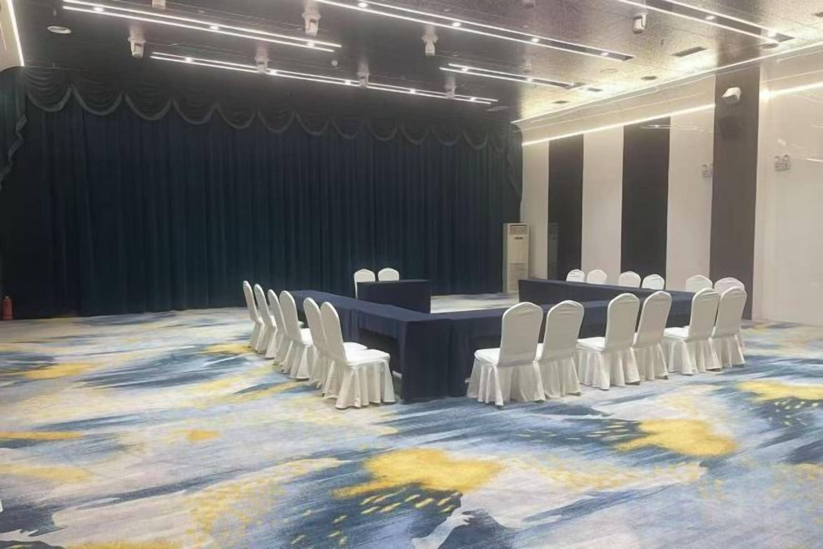 Uma sala de conferências com palco, uma mesa longa e cadeiras dispostas ao redor.